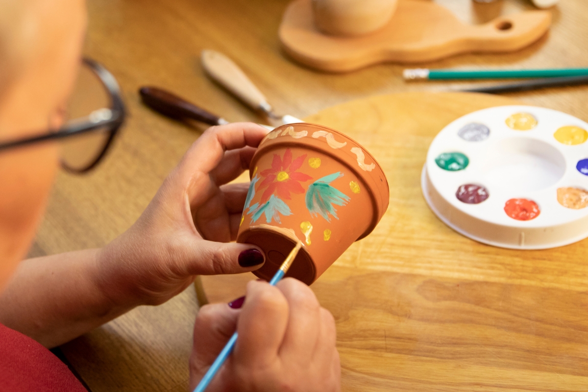 A person painting flowers on a small terracotta plant pot.